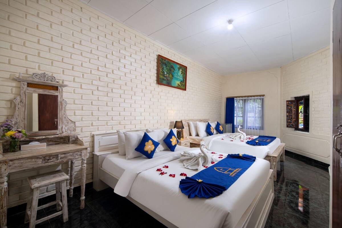 A hotel room with two beds, white brick walls, a wooden desk, a mirror, and a painting on the wall.