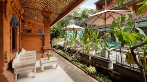 An outdoor seating area with wooden benches and tables, surrounded by potted plants and umbrellas. - Hotel Lumbung Sari Legian (Legian)