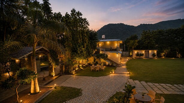 A well-lit outdoor area with a paved walkway, seating arrangements, and a building with multiple windows. - Banjara Hills Resort (Udaipur)