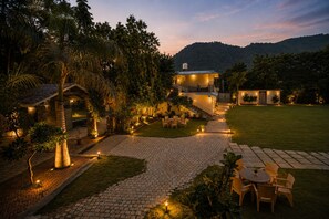 A well-lit outdoor area with a paved walkway, seating arrangements, and a building with multiple windows. - Banjara Hills Resort (Udaipur)