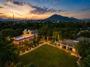 A residential area with a large house featuring a spacious lawn, a swimming pool, and a mountain in the background. - Banjara Hills Resort (Udaipur)