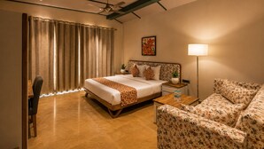 A hotel room with a bed, a sofa, a desk, and a lamp. - Banjara Hills Resort (Udaipur)