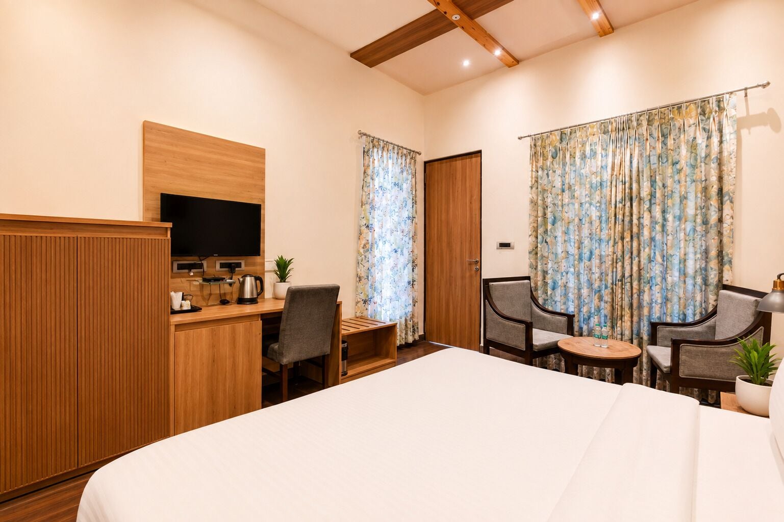 A hotel room with a bed, a desk with a TV, a coffee maker, and two chairs.