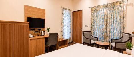 A hotel room with a bed, a desk with a TV, a coffee maker, and two chairs.