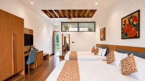 Habitación de hotel con un escritorio de madera, dos camas con ropa de cama floral, un ventanal grande y un techo con listones de madera.