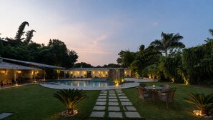 A backyard with a swimming pool, a covered patio area, and a stone pathway leading to a seating area. - Banjara Hills Resort (Udaipur)