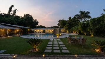 A backyard with a swimming pool, a covered patio area, and a stone pathway leading to a seating area.