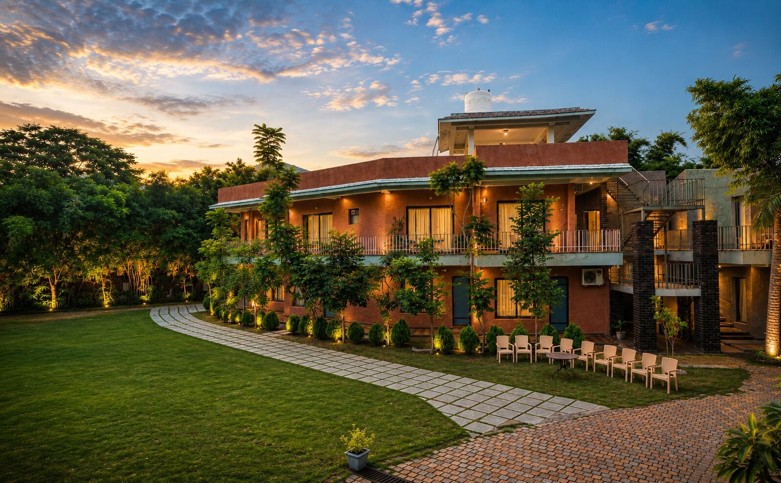 A multi-story hotel with a well-maintained lawn, outdoor seating area, and a water tank on the roof.