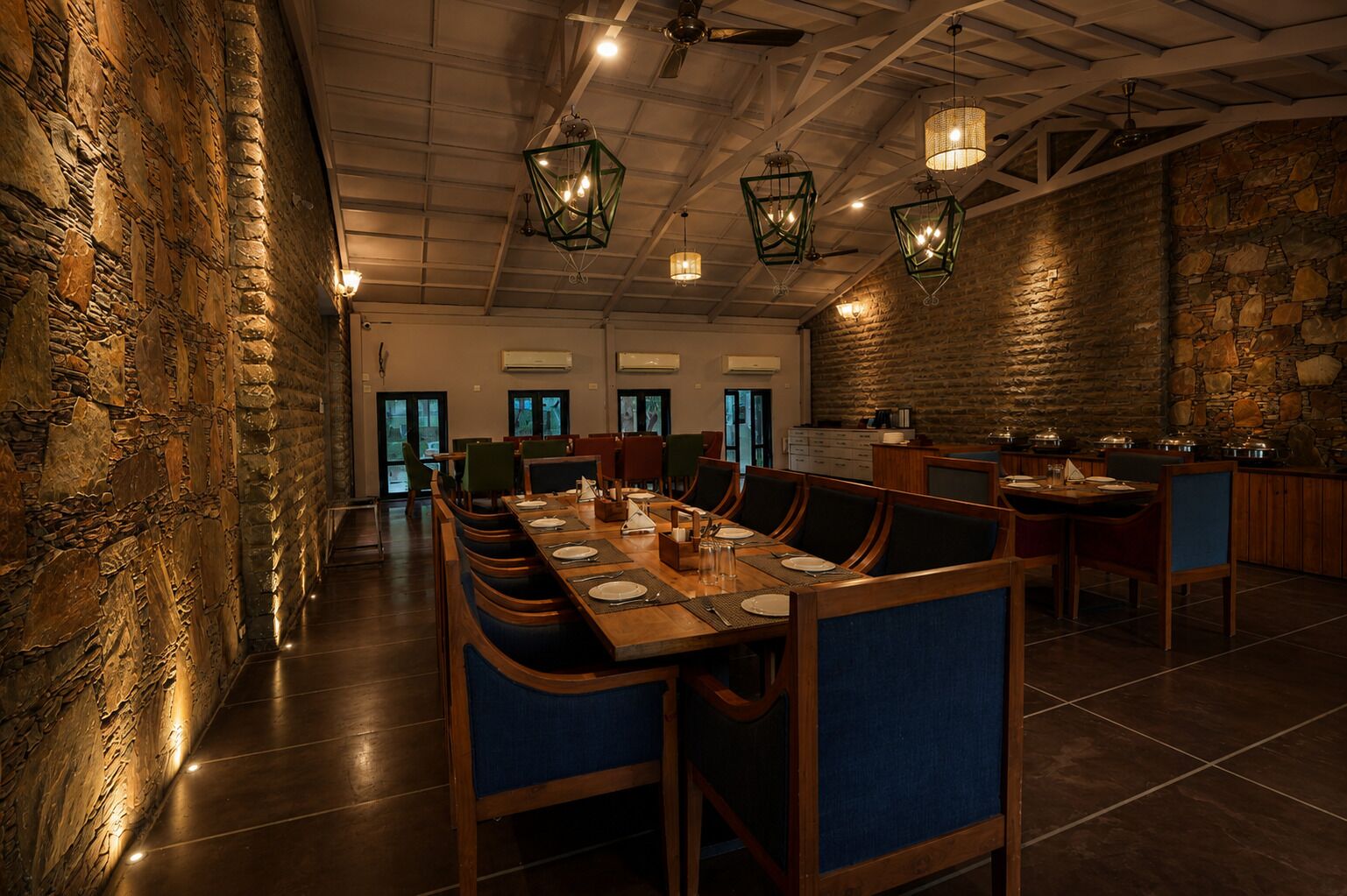 A restaurant with a long communal table, high ceilings, and stone walls.