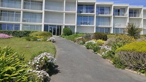 A multi-story hotel with balconies, a central entrance, and a landscaped garden with various plants. - Studio Quiberon Face Mer vue sur les Îles (Quiberon)