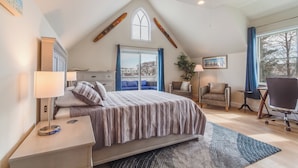 Een slaapkamer met een bed, nachtkastjes, een bureau, een stoel, een raam en een plafondventilator.