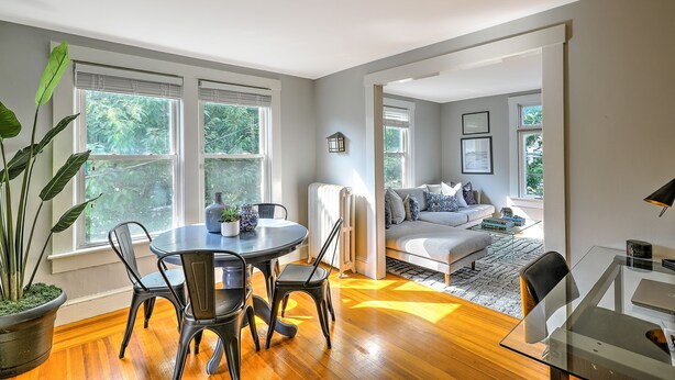 A modern living room with a glass dining table, black chairs, a sofa, and a large window with blinds. - Private Gem in Heart of Downtown Newport  (Newport)