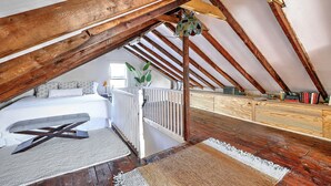 A loft bedroom with a sloped ceiling, wooden beams, a bed, a bench, and a small staircase. - Private Gem in Heart of Downtown Newport  (Newport)