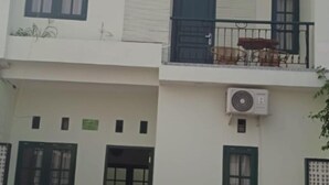 Ein zweistöckiges Gebäude mit einem Balkon im oberen Geschoss, einer Tür mit grünem Rahmen und einem abgestellten Motorrad.