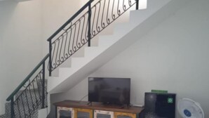 Eine Treppe mit schwarzer Geländer, eine Holzkabine mit Schubladen, ein Fernseher und ein weißer Ventilator.