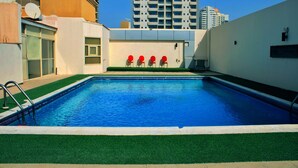 Une piscine à l’eau d’un bleu cristallin, entourée d’une pelouse verdoyante et d’un mur blanc.
