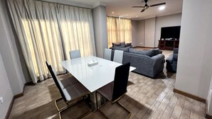 Un salon moderne avec un coin repas, comprenant une table à plateau en verre, des chaises foncées, un canapé gris et un ventilateur de plafond.