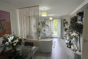 A modern living room with a glass dining table, a hanging chair, and a large window with natural light.