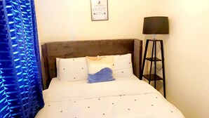 A hotel room with a bed, a headboard, a bedside table with a lamp, and a 'Be Our Guest' sign on the wall.