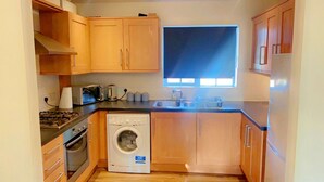 A compact kitchen with wooden cabinets, a washing machine, a stove, and a window providing natural light.