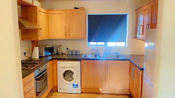 A compact kitchen with wooden cabinets, a washing machine, a stove, and a window providing natural light. - Stunning 2-bed Apartment in London (London)