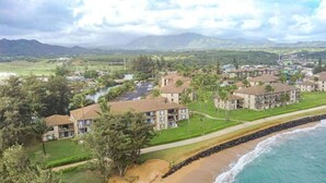 A coastal hotel with multiple buildings, a beach, and a view of distant mountains. - Garden View Suite  Pono Kai Resort PK-K303 (Kapaʻa)