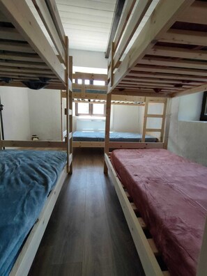 Une chambre avec un lit superposé, un plancher en bois et une fenêtre qui laisse entrer la lumière naturelle.