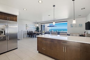 A modern kitchen with a large island, stainless steel appliances, and a dining area with a view.