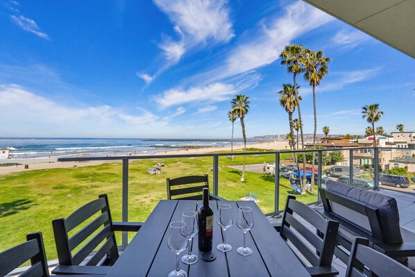 Una mesa con una botella y copas, con vista a una playa con palmeras y cielo despejado.