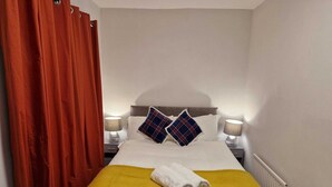 A hotel room with a bed, two pillows, a yellow blanket, a white towel, and a red curtain. - Chester Le Street's Emerald 3 Bed House (Chester-le-Street)