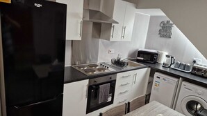A modern kitchen with a black refrigerator, white cabinets, a stainless steel range hood, a sink with a dish rack, a microwave, a toaster, and a washing machine. - Chester Le Street's Emerald 3 Bed House (Chester-le-Street)