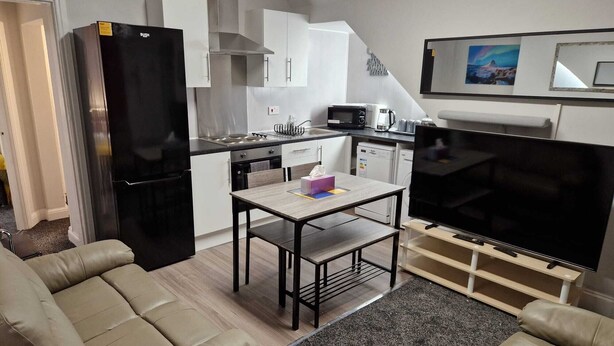 A compact living space with a kitchenette, a dining area, and a seating area with a TV. - Chester Le Street's Emerald 3 Bed House (Chester-le-Street)