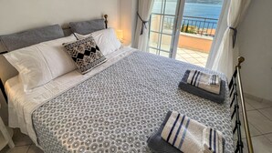 A bedroom with a bed, pillows, a patterned bedspread, and a view of the sea through a window. - Villa Fortuna in Nikiana (Lefkada)