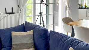 A modern living room with a blue sofa, a telescope, and a dining area with a table and chairs. - Villa Fortuna in Nikiana (Lefkada)