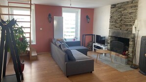 Ein Wohnzimmer mit grauem Sofa, Kamin aus Stein, Fernseher und einer Treppe.