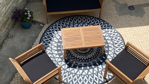 Ein runder Sitzbereich im Freien mit einem gemusterten Teppich, einem Holztisch und zwei Holzsesseln mit Kissen.