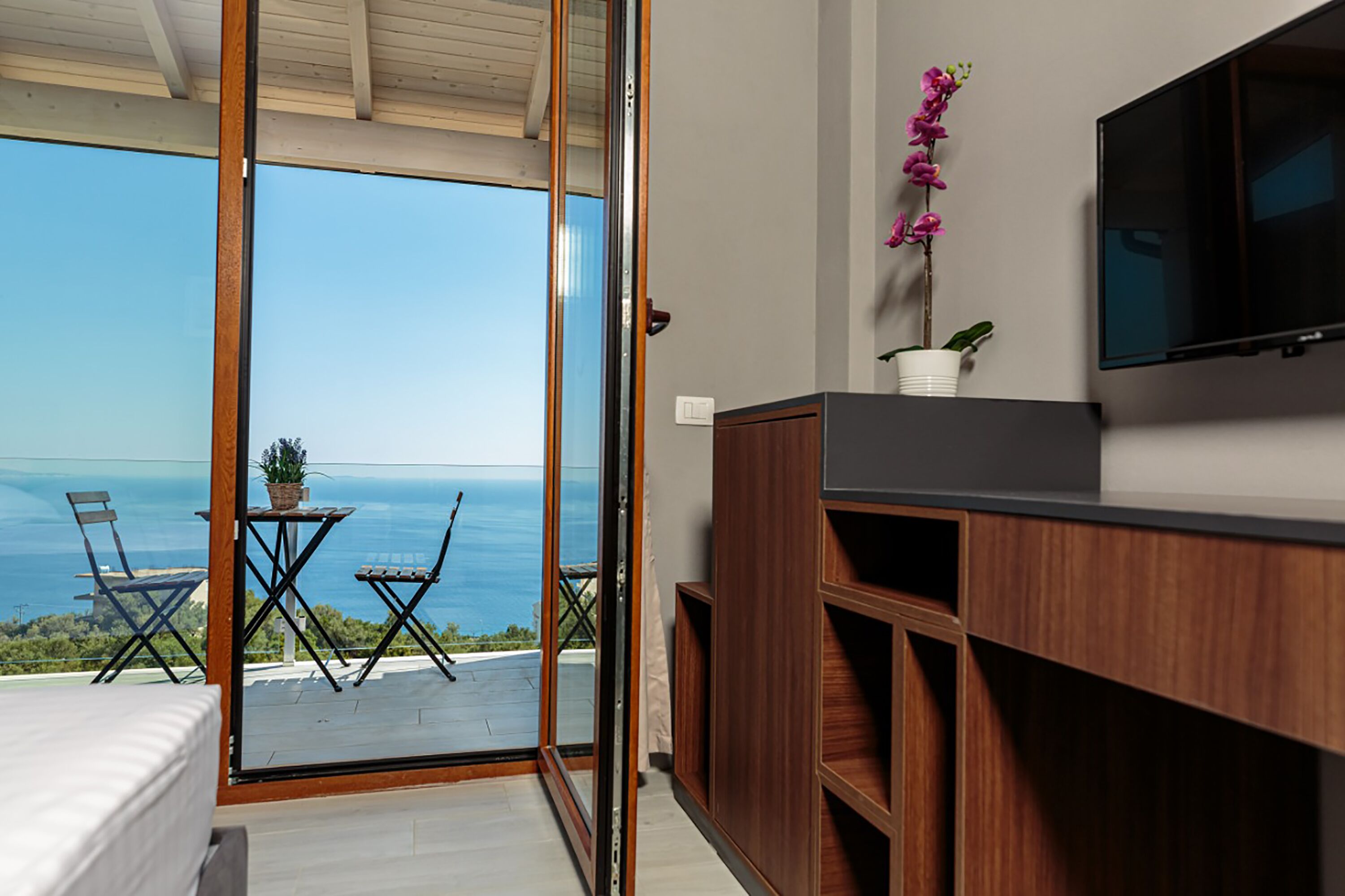 A modern room with a sliding glass door leading to a balcony with a view of the sea.
