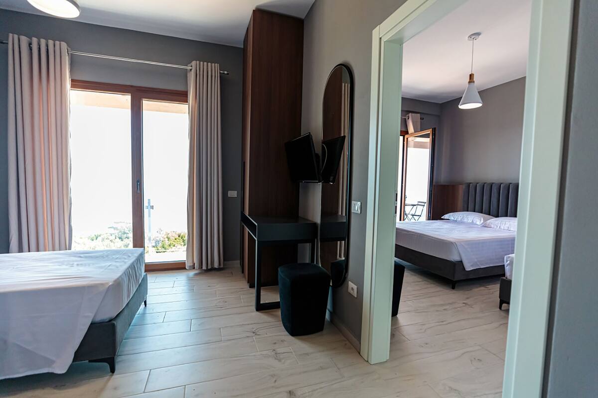 A hotel room with two beds, a small table, a TV, and a view of the outdoors.