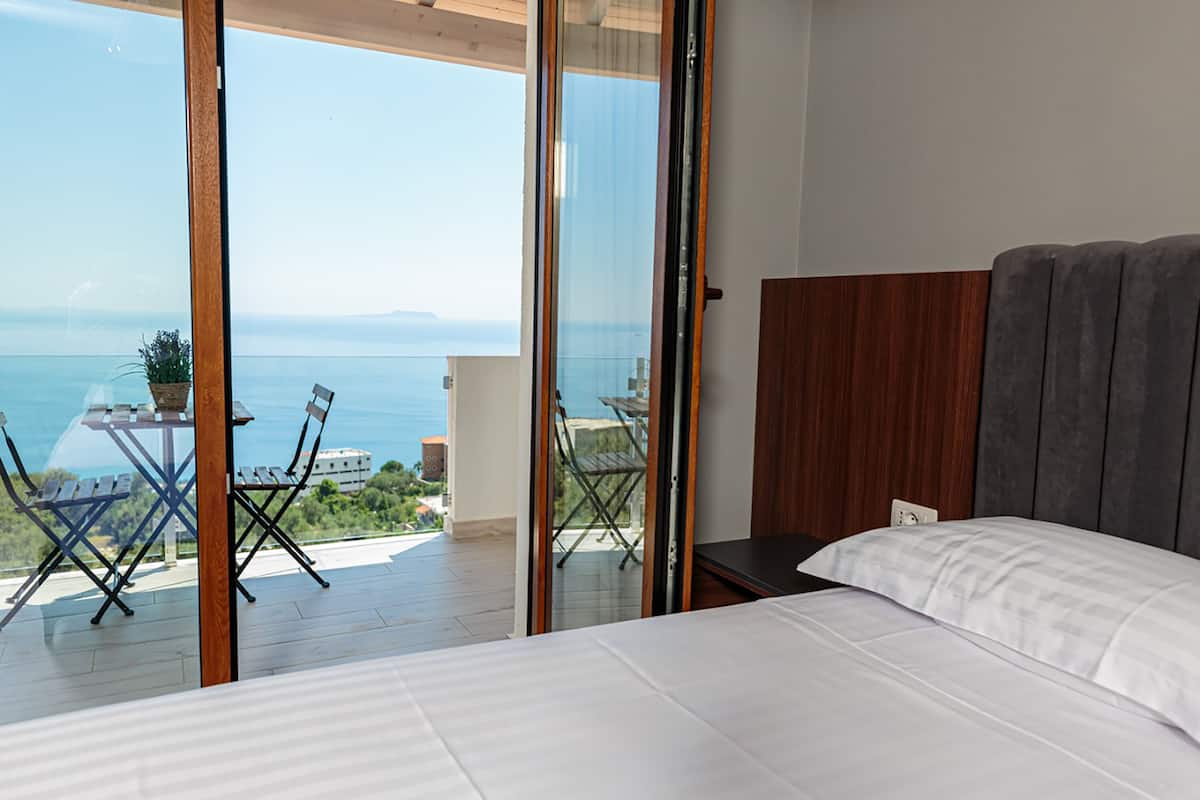A bedroom with a large bed, a view of the sea, and a balcony with a table and chairs.