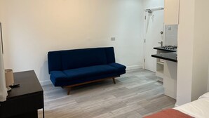 Un espace de vie compact comprenant un canapé bleu, une petite table d’appoint noire et un coin cuisine équipé d’une cuisinière et d’un évier.