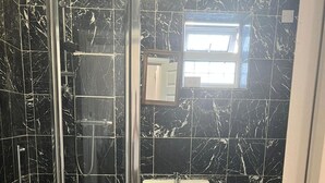 Une salle de bain avec une douche à parois de verre, un lavabo blanc et des toilettes adossées à un mur en marbre noir.