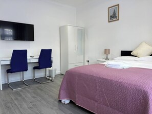 A hotel room with a bed, a desk with two chairs, a wardrobe, a television, and a framed picture on the wall. - Remarkable 2-bed Apartment in Ilford, London (Ilford)