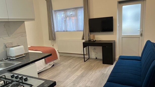 Une pièce compacte comprenant un coin cuisine, un lit, un bureau, une télévision et un canapé bleu.