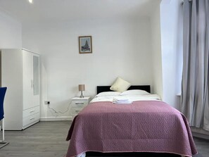 A bedroom with a bed, a nightstand, a lamp, a wardrobe, and a picture on the wall. - Remarkable 2-bed Apartment in Ilford, London (Ilford)