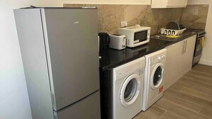 Une cuisine compacte équipée d’un réfrigérateur, d’un four à micro-ondes, d’un grille-pain et d’un lave-linge.