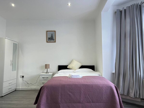 A bedroom with a bed, a nightstand, a lamp, a wardrobe, and a framed picture on the wall. - Remarkable 2-bed Apartment in Ilford, London (Ilford)