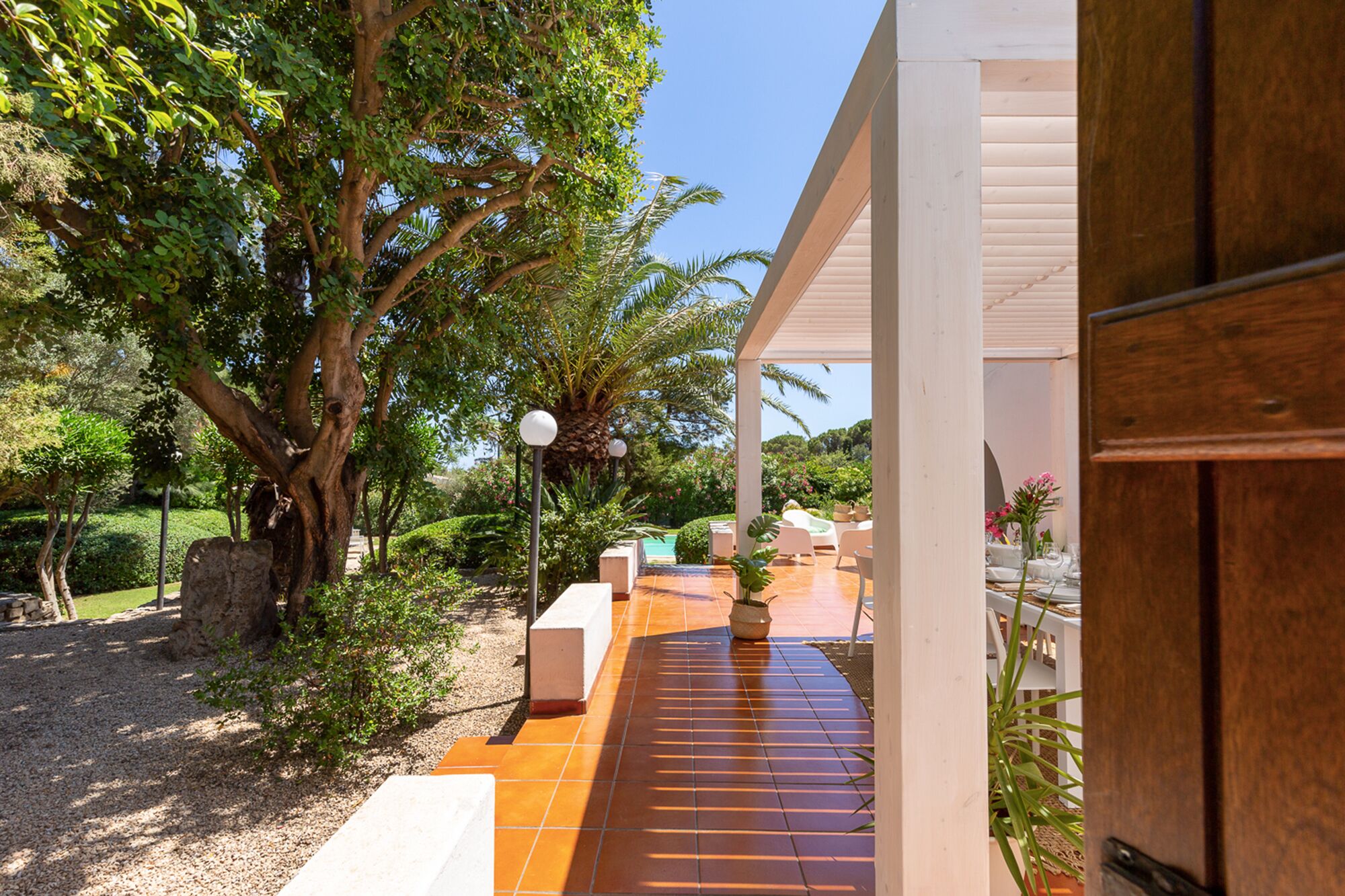 A covered outdoor area with a tiled patio, a stone bench, and a potted plant.