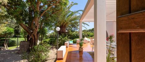 A covered outdoor area with a tiled patio, a stone bench, and a potted plant.