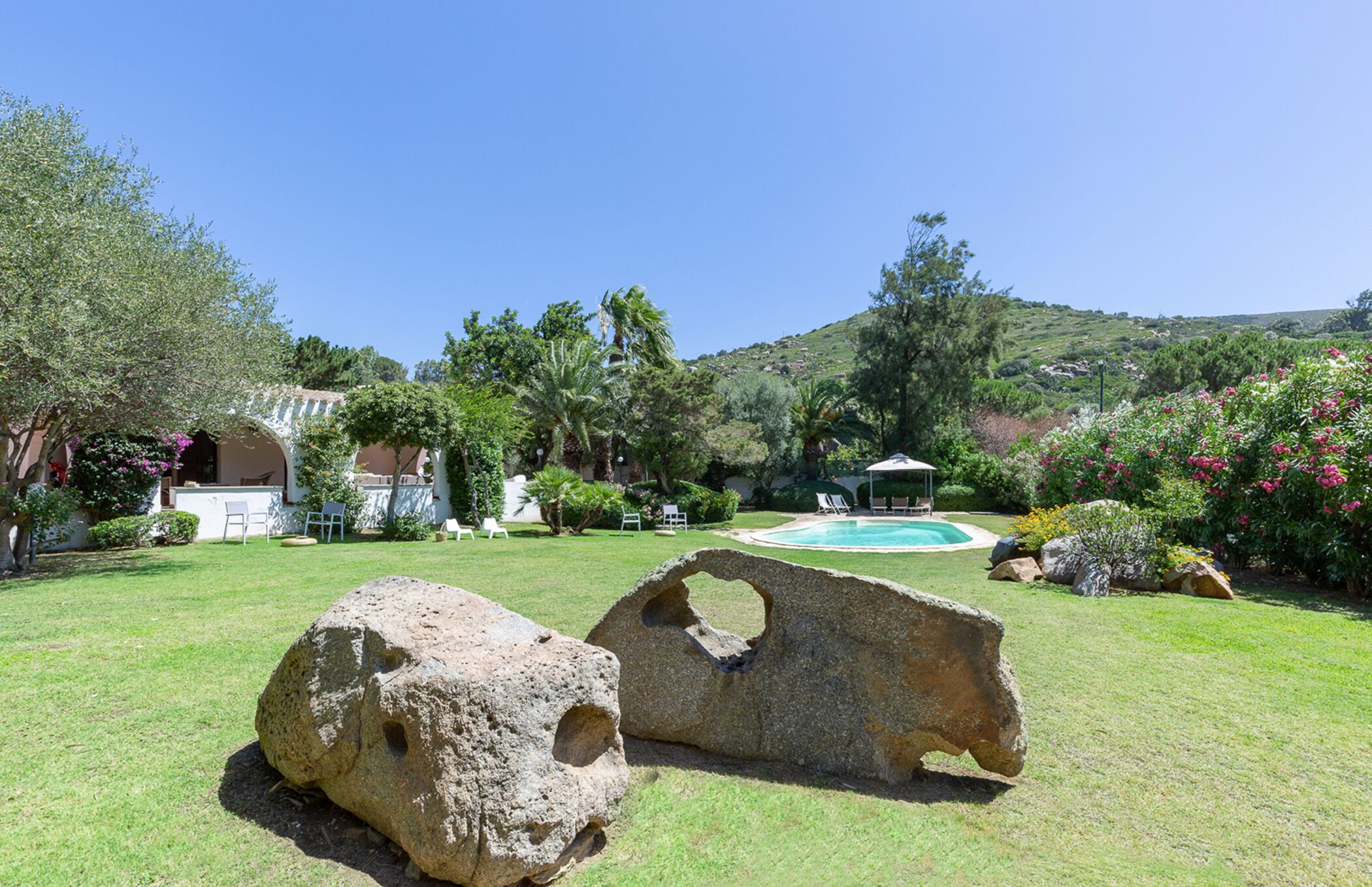 Un jardín ajardinado con piscina, rocas grandes y mobiliario para exteriores.