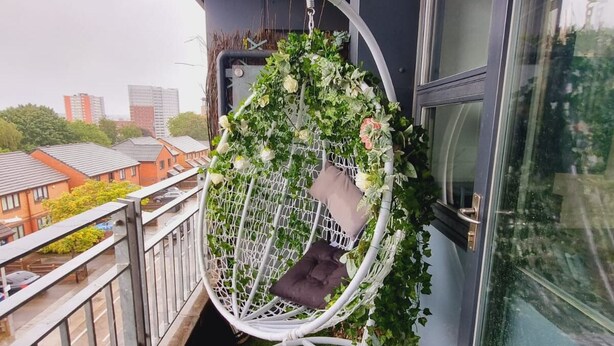 A white hanging chair with a cushion, surrounded by greenery, on a balcony with a view of buildings. - Bull's Ring 3bed Penthouse City Centre (Birmingham)